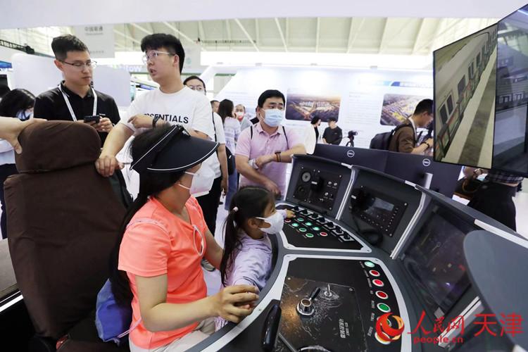 一位參觀者和孩子在天津軌道交通集團(tuán)展臺(tái)體驗(yàn)智能駕駛帶來的樂趣。人民網(wǎng)記者 孫翼飛攝